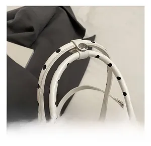 Close-up of white polka dot handbag handle with metal snap fastener and stitching