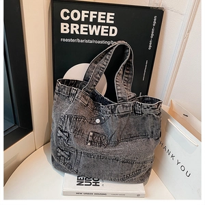 Detail view of deconstructed gray denim tote bag with vintage stitching on white table