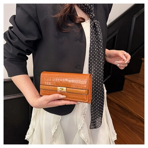 Pochette marron à motif crocodile avec fermoir rotatif doré portée avec une tenue élégante