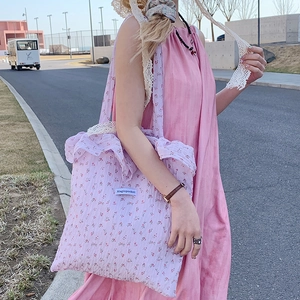 Pink floral tote bag with lace straps and ruffled edges shown in a stylish outdoor setting