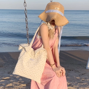 Women's floral canvas tote bag and woven straw hat styled for a beach vacation