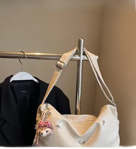Detail of cream hobo bag with silver butterfly metal studs and a plush bear charm