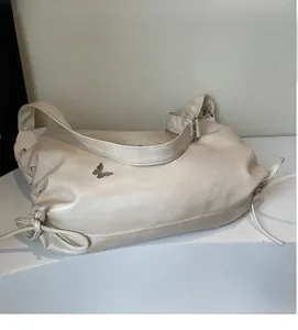 Detail of off-white faux leather tote bag with silver butterfly charm and side drawstrings