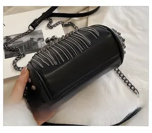 Detail of black cylindrical crossbody bag featuring dense metal fringe and side rivets