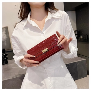 Détail d'un long portefeuille rouge gaufré crocodile avec boucle dorée tenu par un mannequin