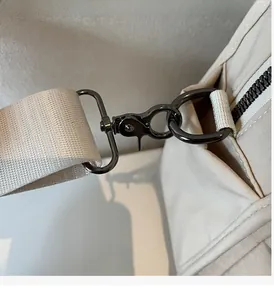 Detail of durable gunmetal hardware hook and beige woven shoulder strap on the bag