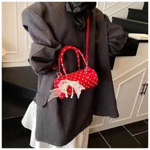 Macro detail of red polka dot cylinder bag with white lace bow and pearl pendant charm