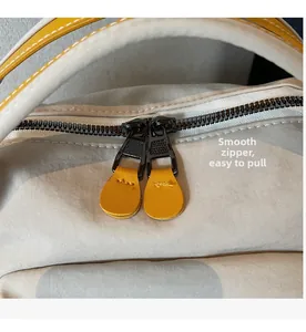 Detail of smooth metal double zippers with yellow leather pulls and fine stitching