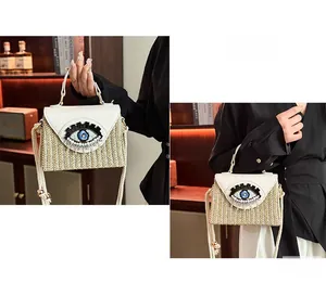 Detail of hand-woven straw bag featuring evil eye embroidery and white leather flap cover