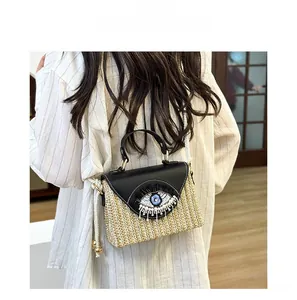 Close-up of woven straw bag with sequined eye detail and detachable rope shoulder strap