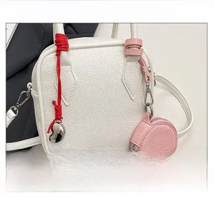 Detail view of white lychee leather handbag featuring heart charm and mini round pouch