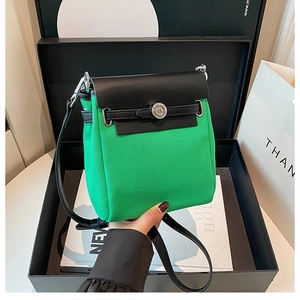 Detail of green canvas crossbody bag with black leather trim and silver metal buckle