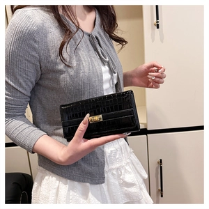 Détail d'une pochette noire à motif crocodile avec fermoir rotatif rectangulaire doré poli