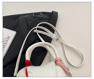 Detail of white litchi leather handbag featuring woven red handles and adjustable strap