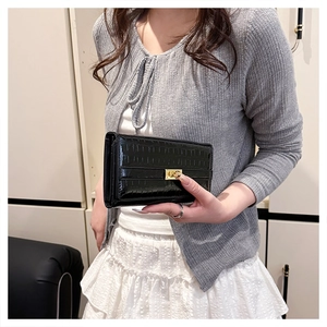Détails de la texture crocodile noire et du fermoir tournant doré sur une pochette femme