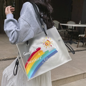 Clear PVC tote bag with rainbow print and black leather straps shown in outdoor setting