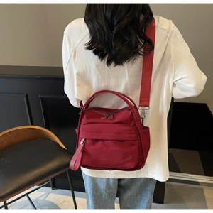 Model showing a burgundy canvas tote bag with wide straps in a minimalist indoor setting