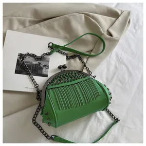 Detail of bright green crossbody bag with metal studs, fringe chains, and clasp closure