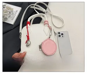 Close-up of white pebble leather crossbody bag with heart charm and phone for size reference