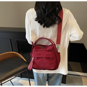 Deep red lightweight crossbody bag with adjustable wide fabric strap on casual outfit