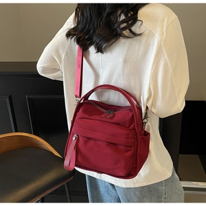 Detailed view of burgundy nylon crossbody bag with multiple zip pockets on a female model