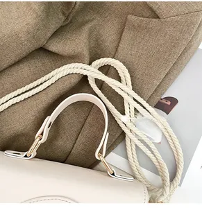 Detail of woven rope strap and leather handle with light gold metal rings on a cream bag