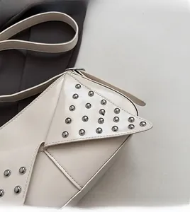 Detail view of beige underarm bag showing silver rivets and triangular flap texture