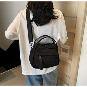 Detail of the black nylon crossbody bag showing the waterproof fabric and zipper pocket