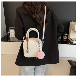 Close-up of a white lychee grain leather crossbody bag with a pink mini coin purse charm