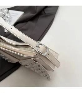 Detail of silver rivets and metal buckle on beige leather punk style underarm bag