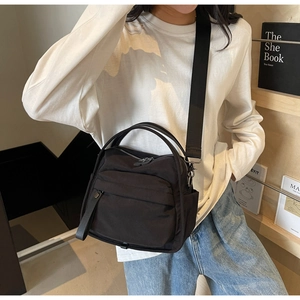 Detail of a black nylon crossbody bag with zipper pockets and adjustable wide shoulder strap