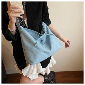 Detail of light blue denim tote bag featuring white cursive embroidery and drawstring bow