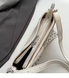Detailed close-up of smooth metal zipper and silver studs on a beige shoulder bag