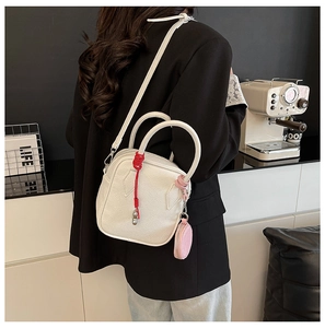 White lychee leather handbag detail with red woven fringe and pink round pendant