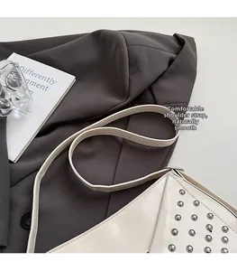 Detail of silver rivets on a cream-white leather crossbody bag with broad strap