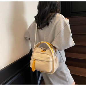 Detail of canvas square bag featuring yellow webbing handles and front zipper pocket