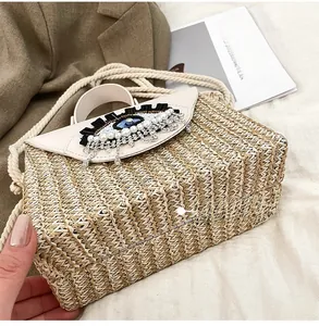 Detail showing woven straw bag base with white leather flap and pearl eye embroidery