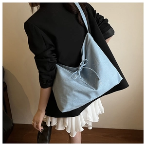 Detail of light blue denim tote bag featuring a bow tie and glittery lettering embroidery