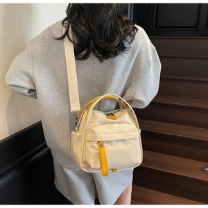 Detail of minimalist cream canvas crossbody bag with yellow accents shown on a model