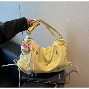 Detailed view of yellow hobo bag with butterfly hardware and plush charm on art books
