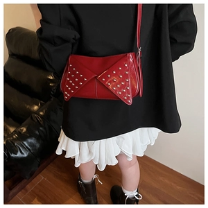 Détail du sac bandoulière en cuir verni rouge avec rivets argentés et rabat enveloppe