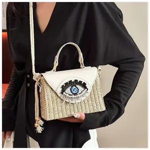 Detail of evil eye embroidery with blue beads and pearl fringe on straw crossbody bag