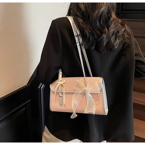 Dettaglio di una borsa a spalla rosa con fiocco in pizzo e finitura lucida su modella