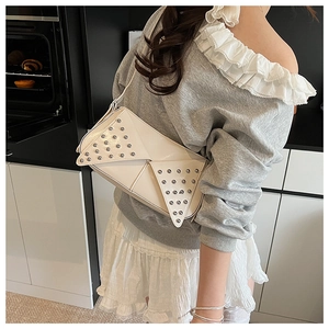 Détail d'un sac à bandoulière en cuir blanc avec des rivets argentés et motifs géométriques