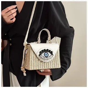 Detail of evil eye embroidery with pearl tassels on a woven straw handbag with leather flap