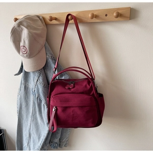 Detail of burgundy canvas tote bag with functional pockets hanging on a wooden wall hook