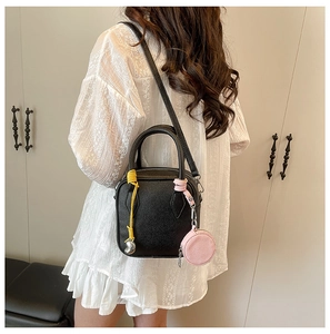 Detail of black lychee texture crossbody bag with yellow tassel and pink coin purse