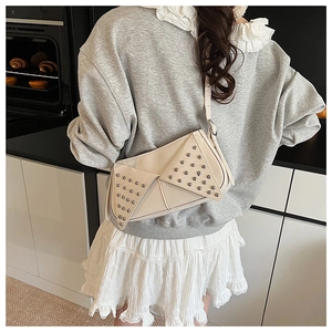 Detail of beige leather square bag with silver rivets worn over a grey sweatshirt