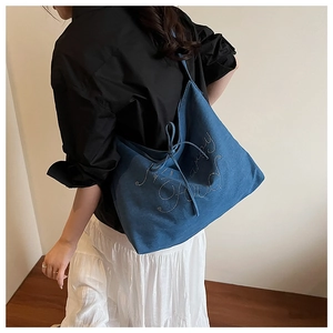 Detail of a large denim tote bag with rhinestone lettering and knot accents on model
