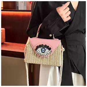 Detailed view of handmade woven straw bag with pink leather flap and beaded evil eye embroidery
